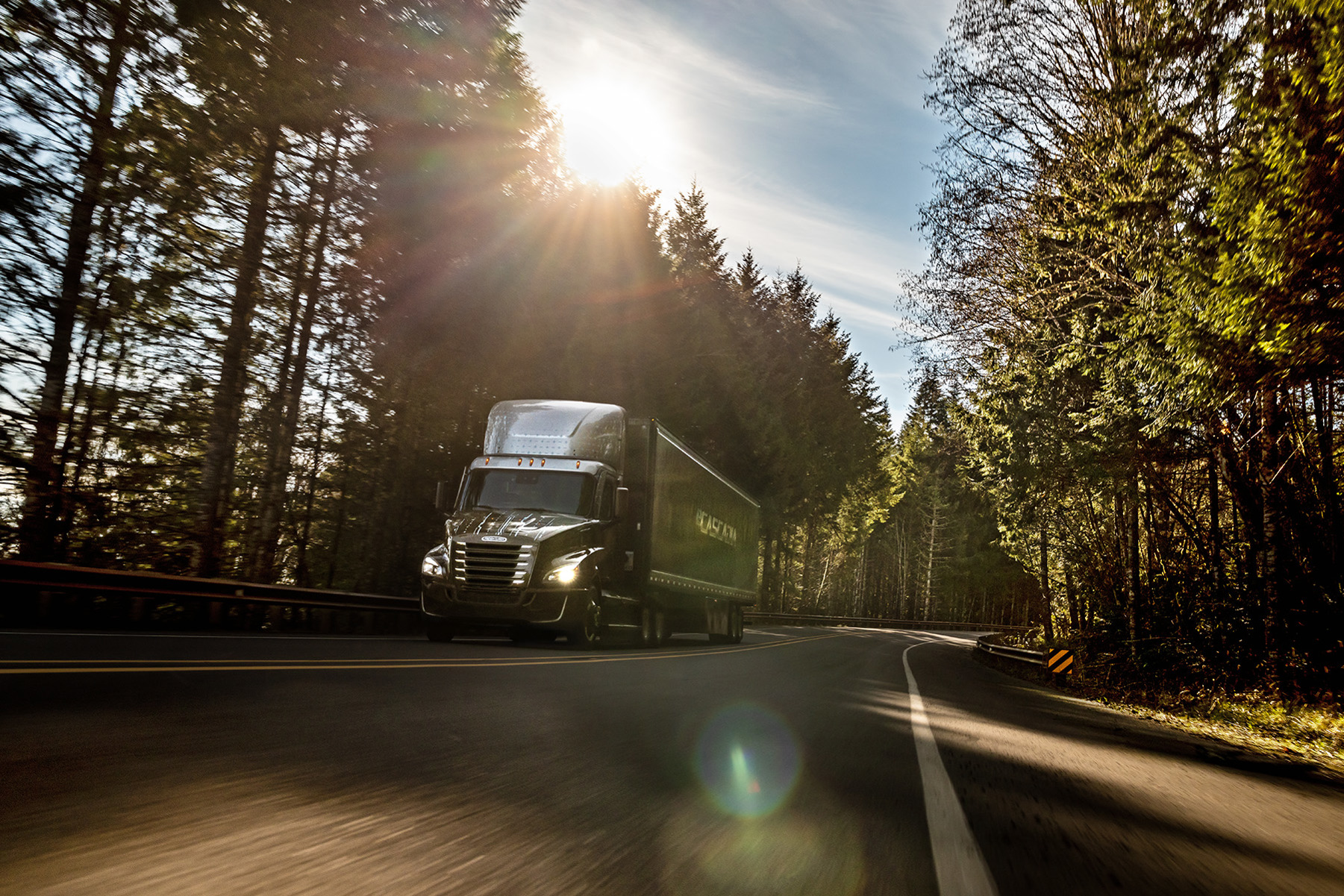 A Freightliner eCascadia semi-truck is driving on a road. 