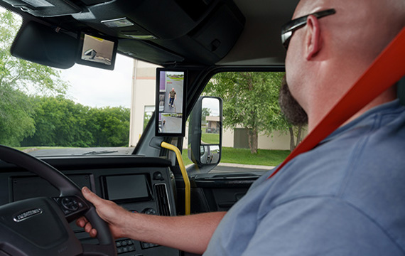Freightliner truck cab interior view with driver operating steering wheel and digital dashboard display